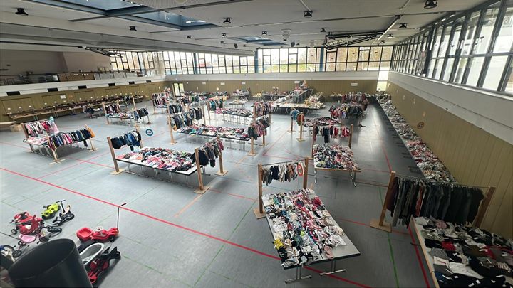 Helle Flohmarkthalle mit nach Größen sortierten Tischen und Kleiderständern